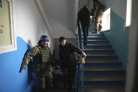 A Ukrainian serviceman and a civilian carry a wounded man who was injured by shelling in a hospital in Mariupol, Ukraine. (Photo | AP)