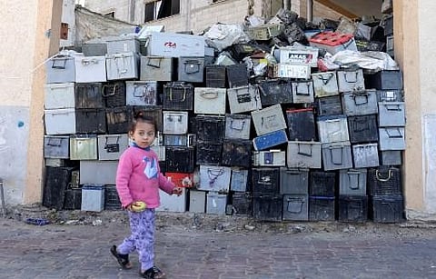 A Palestinian girl walks past a stack of discarded batteries slated for recycling in Khan Yunis in the southern Gaza Strip, on February 14, 2022. (Photo | AFP)