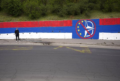 A man waits at a bus station by a wall that shows the colors of the Serbian flag and graffiti against EU and NATO in Belgrade, Serbia, Wednesday, March 30, 2022. (Photo | AP)