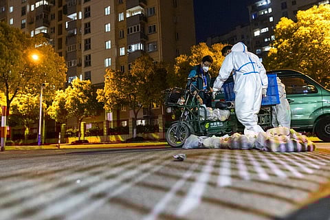 Deliverymen wearing protective suits carry bags of food at the gate of a residential community in Shanghai, China, Monday, April 11, 2022(Photo | AP)