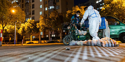 Deliverymen wearing protective suits carry bags of food at the gate of a residential community in Shanghai. (Photo| AP)