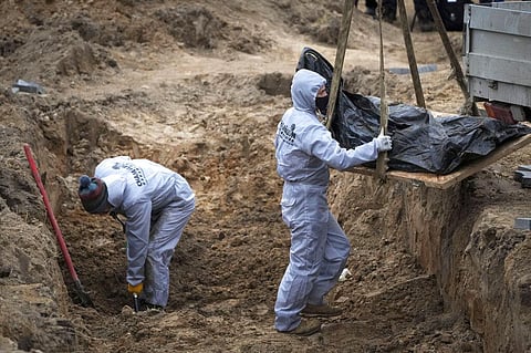 Men wearing protective gear exhume the bodies of civilians killed during the Russian occupation in Bucha, on the outskirts of Kyiv. (Photo | AP)