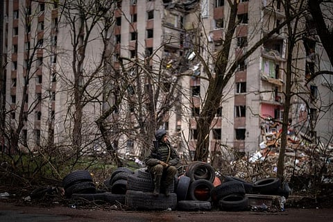 A Ukrainian soldier sits on tyres next to a building destroyed by Russian bombing in Chernihiv. (Photo | AP)