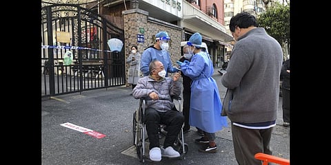 Workers in protective gear help a man in a wheelchair during the mass testing for residents in a lockdown area in the Jingan district of western Shanghai on April 4, 2022. (Photo | AP)