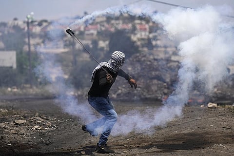 A Palestinian demonstrator hurls back a tear gas canister fired by Israeli forces during a protest against the West Bank Jewish settlements. (Photo | AP)
