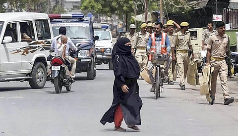 A Muslim woman walks on a street as security personnel conduct a flag march, a day after clashes during protest against remark on Prophet Muhammad, in Prayagraj. (Photo | PTI)