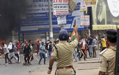A policeman aims to fire in the air to disperse people protesting against Centre's 'Agnipath' scheme, in Danapur, Friday, June 17, 2022. (Photo | PTI)