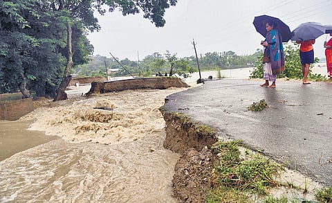 Locals look at a section of a road washed away by flood waters at Dhamdhama in Nalbari district of Assam on Friday. (Photo | PTI)