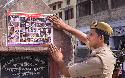 A police person sticks a poster of those accused to be involved in a clash following a controversial remark by suspended BJP leader Nupur Sharma, in Kanpur. (Photo | PTI)