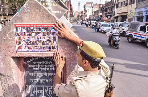 A police person sticks a poster of those accused to be involved in a clash following a controversial remark by suspended BJP leader Nupur Sharma, in Kanpur. (Photo | PTI)