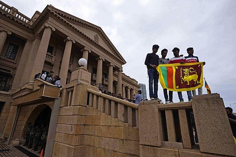People stand holding a national flag at the President Gotabaya Rajapaksa's office on the second day after it was stormed in Colombo. (Photo | AP)