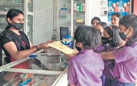 Students hand over paper bags to a shop owner in Kaloor