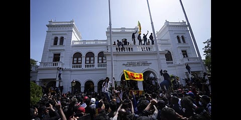 A protester, carrying national flag, stands with others on top of the building of Sri Lankan Prime Minister Ranil Wickremesinghe's office(PTI)