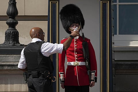 A police officer givers water to a British soldier wearing a traditional bearskin hat, on guard duty outside Buckingham Palace, during hot weather in London. (Photo | AP)