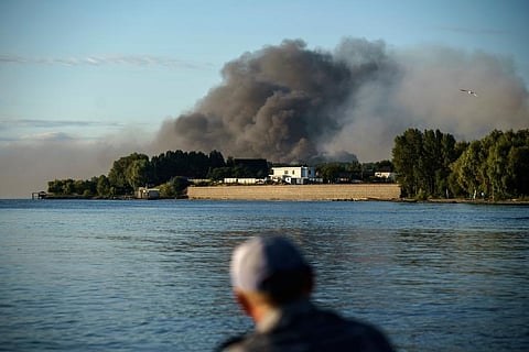 A fisherman watches smoke rise after Russian forces launched a missile attack on a military unit in the Vyshhorod district on the outskirts of Kyiv, Ukraine. (Photo | AP)