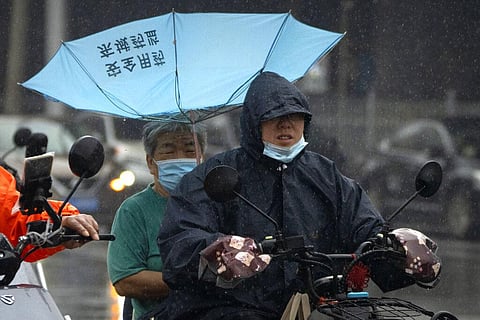 Men wearing face masks ride on a scooter under an upturned umbrella in the rain in Beijing, Thursday, Aug. 18, 2022.(Photo | AP)