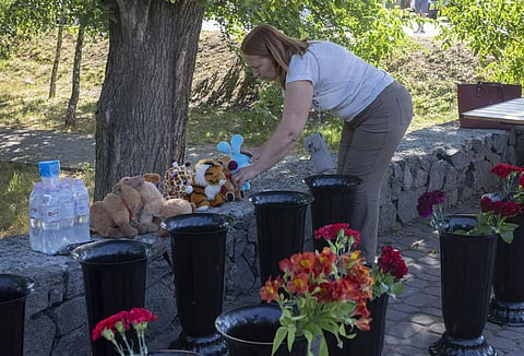 A woman lays a toy at a shopping center burned after a rocket attack in Kremenchuk, Ukraine. (Photo |AP)