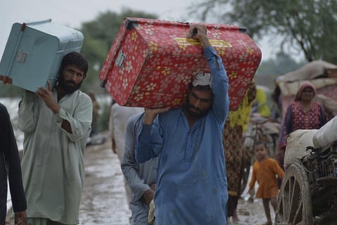Displaced people carry belongings after they salvaged usable items from their flood-hit home as they wade through a flooded area in Jaffarabad, a district of Pakistan. (Photo | AP)