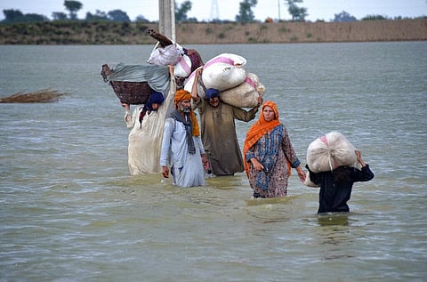 A displaced family wades through a flooded area after heavy rainfall, in Jaffarabad, a district of Pakistan's southwestern Baluchistan province. (Photo | AP)