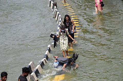 Pedestrians use a road divider on a flooded stretch on the Outer Ring Road on Tuesday. (Photo | Nagaraja Gadekal, EPS)