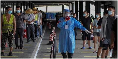 A volunteer in protective gears uses a loud speaker to advise people to keep social distancing at a COVID-19 testing site in Sanya. (Photo | AP)