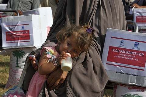 A baby girl drinks milk while she stands beside her mother waiting to receive food and other items distributed by the religious charity group Al-Khidmat Foundation, Sept 13, 2022. (Photo | AP)