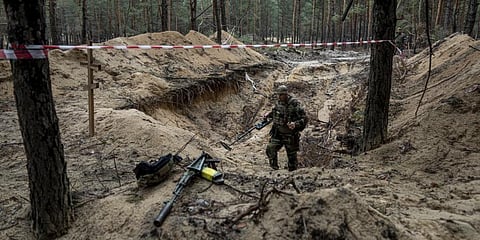 A Ukrainian serviceman uses a metal detector to inspect a mass grave in the recently retaken area of Izium, Ukraine, Thursday, Sept. 15, 2022 .(Photo | AP)