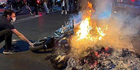 A man pulls out a police motorcycle which is set on fire during a protest over the death of a young woman who had been detained for violating the country's conservative dress code. (Photo |AP)