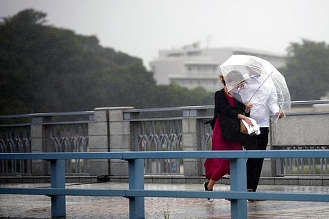 People share an umbrella against strong wind and rain as they walk on a bridge in Kawasaki, near Tokyo. (Photo | AP)