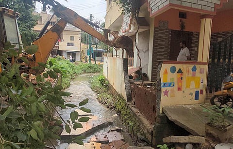 A bulldozer deployed by BBMP demolishes a portion of a house for encroaching a storm water drain at Mahadevapura in Bengaluru on Saturday | Express