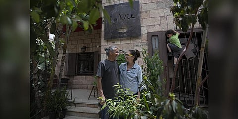 Kenae Totah, 5, right, plays while his parents Morgan Cooper, 41, center and foreign spouse Saleh Totah, right, pose for a photo in front of their restaurant, at the West Bank city of Ramallah. (Phot