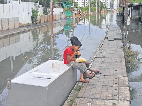 Children eat seated on a defunct refrigerator on a flooded street in Bellandur | Vinod Kumar T