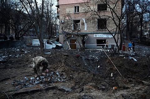 A serviceman collects fragments of missile in a crater left by a Russian strike in front of a residential building in the Ukrainian capita Kyiv on December 31, 2022. (Photo | AP)