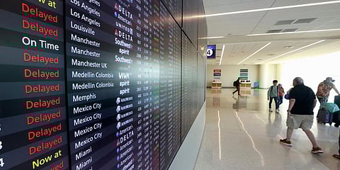 Passengers walk past s flight status board in Terminal C at Orlando International Airport that shows many delays. (Photo | AP)