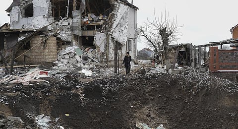 A woman stands on top of a crater next to a destroyed house after a Russian rocket attack in Hlevakha, Kyiv region. (Photo | AP)