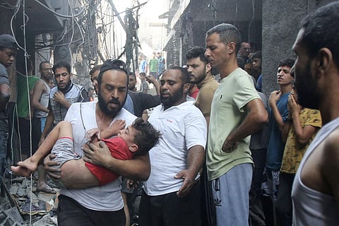 A Palestinian man rushes past rubble carrying a child in his arms, following an Israeli military strike, as raging battles between Israel and the Hamas movement continue. (Photo | AFP)