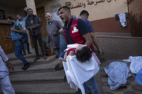 Palestinian medic holds a child killed in the Israeli bombardment of the Gaza Strip in a morgue in Khan Younis, Tuesday, Oct 17, 2023. (Photo | AP)
