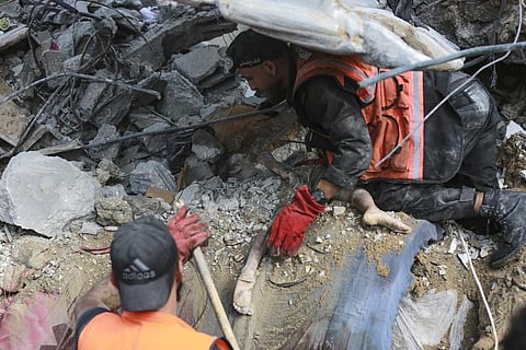 Palestinian rescue members remove the rubble from a body of a dead child was found under a destroyed house after Israeli airstrikes on Gaza City. (Photo | AP)