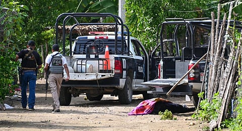 Security forces pass by a corpse as they inspect the area where at least 11 police officers were killed in an ambush by criminal groups. (Photo | AFP)