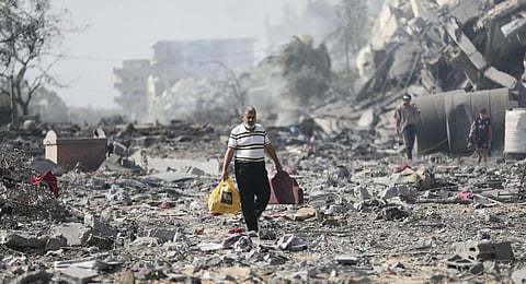 Palestinians walk by buildings destroyed in the Israeli bombardment on al-Zahra, on the outskirts of Gaza City. (Photo | AP)