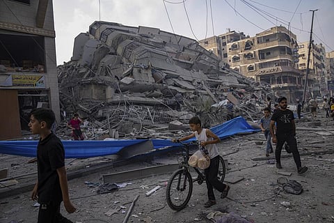 Palestinians walk by the rubble of a building after it was struck by an Israeli airstrike, in Gaza City. (Photo | AP)