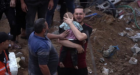 A Palestinian man cries while holding a dead child who was found under the rubble of a destroyed building following Israeli airstrikes in Nusseirat refugee camp, central Gaza Strip. (Photo | AP)