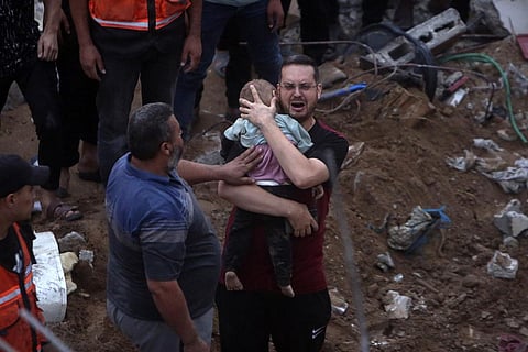 A Palestinian man cries while holding a dead child who was found under the rubble of a destroyed building following Israeli airstrikes in Nusseirat refugee camp. (Photo | AP)