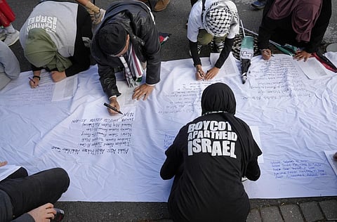 Pro-Palestinian supporters write names of lives lost in the war, as they protest outside Parliament in Cape Town, South Africa, Nov 21, 2023. (Photo | AP)