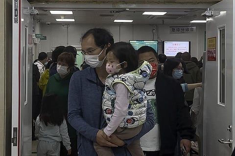 A man carriers a child walk out from a crowded holding room of a children's hospital in Beijing. (Photo | AP)