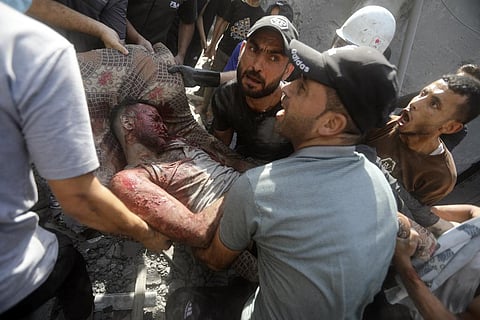 Palestinians carry an injured man after being rescued from under the rubble of a destroyed building following an Israeli airstrike in Bureij refugee camp. (Photo | AP)