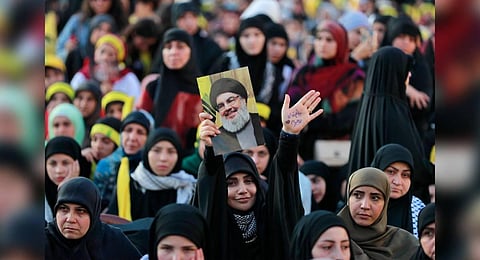A supporter of the Lebanese Shiite movement Hezbollah holds a portrait of its leader Hassan Nasrallah as people watch his televised speech | AFP