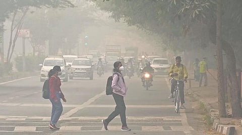 Students wearing masks cross a road amid hazy weather conditions in New Delhi