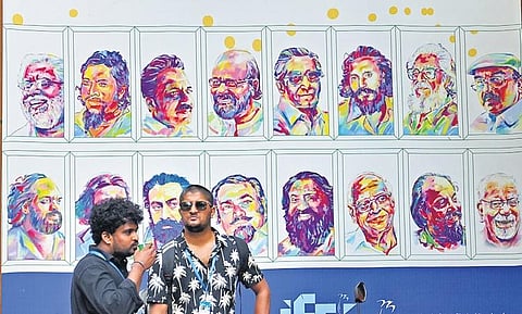 Delegates standing in front of a hoarding that displays photos of legendary Malayalam filmmakers at Tagore Theatre, the main venue of the International film festival in Thiruvananthapuram, on Sunday