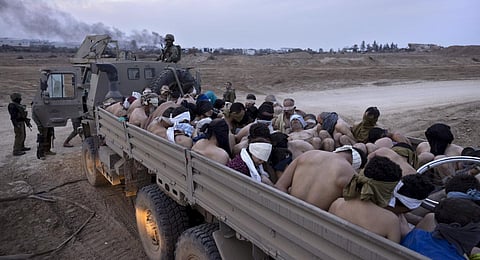 Israeli soldiers stand by a truck packed with bound and blindfolded Palestinian detainees, in Gaza. (Photo | AP)